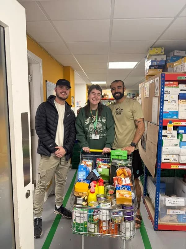 Three people with a trolley of donated food in a store room
